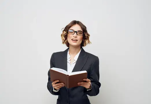 Молодая женщина в очках и деловом костюме читает книгу