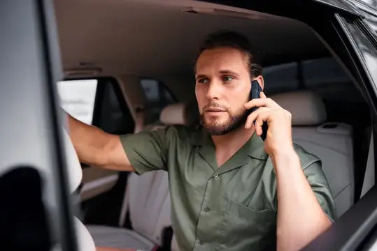 Молодой человек в повседневной зеленой рубашке сидит в автомобиле и разговаривает по телефону