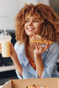 Кудрявая девушка с пиццей и молочным коктейлем улыбается