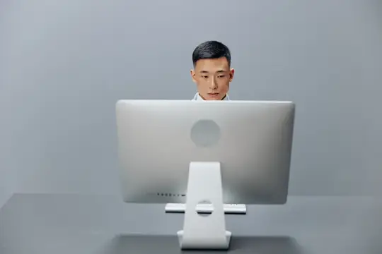 Азиатский мужчина работает за компьютером, сидя за столом в офисе, что отражает деловой образ жизни и работу