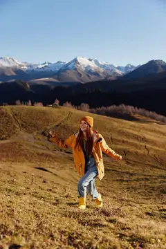 Девушка в жёлтой куртке танцует на фоне снежных гор