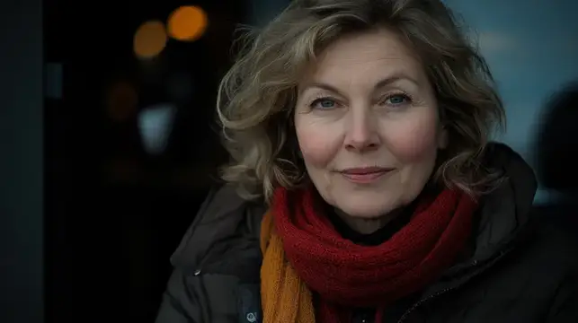 Светловолосая женщина в красном шарфе спокойно смотрит в камеру