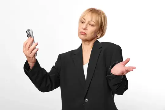 Блондинка в деловом костюме с недоумением смотрит на телефон