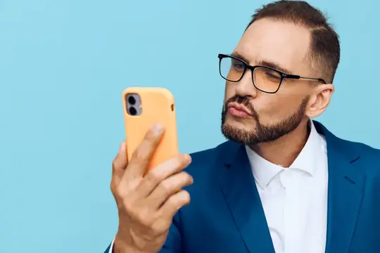 Мужчина в очках и синем пиджаке смотрит на смартфон