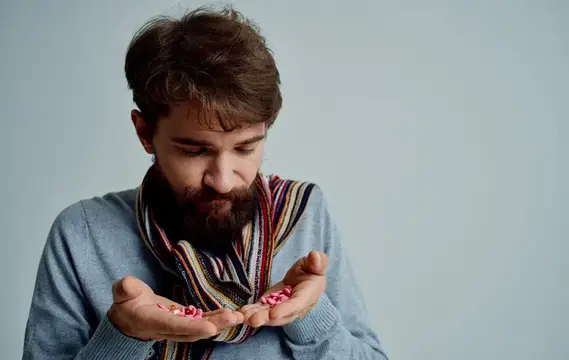 Бородатый мужчина в свитере и шарфе держит горсть конфет