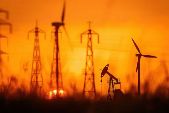 Силуэты нефтяной качалки и ветряков на фоне оранжевого заката