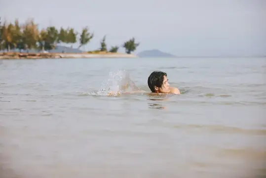 Мужчина плывёт в спокойном море у берега