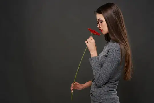 Девушка в очках нюхает красный цветок на тёмном фоне
