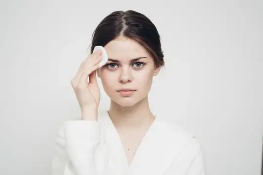 Молодая женщина протирает лицо ватным диском на светлом фоне