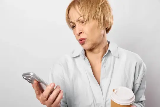 Встревоженная женщина со смартфоном и чашкой демонстрирует стресс, проблемы со здоровьем, беспокойство по поводу общения, крупный план в помещении, держит напиток на вынос, медицинская проблема…