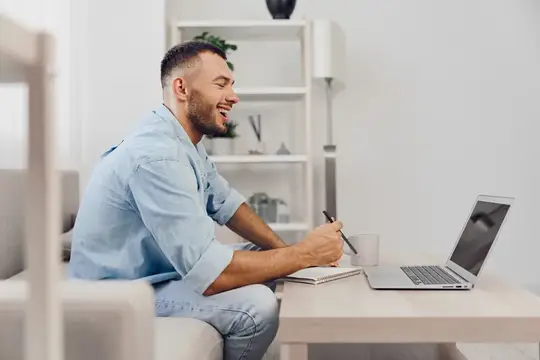 Улыбающийся мужчина с блокнотом работает за ноутбуком дома