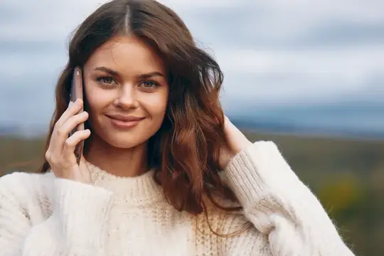 Молодая женщина с тёмными волосами улыбается, разговаривая по телефону на улице