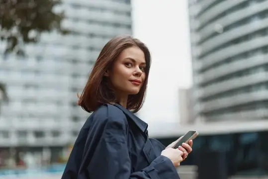 Молодая женщина с телефоном оборачивается на улице города