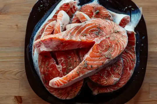 Маринованная красная рыба на тарелке, стоящей на деревянном фоне