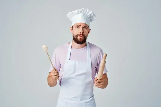 Бородатый мужчина в поварском колпаке с половником и скалкой