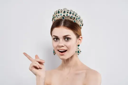 Улыбающаяся девушка в роскошной короне с изумрудами указывает пальцем в сторону