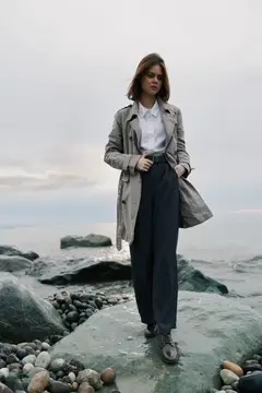 Молодая женщина в плаще стоит на камнях у моря