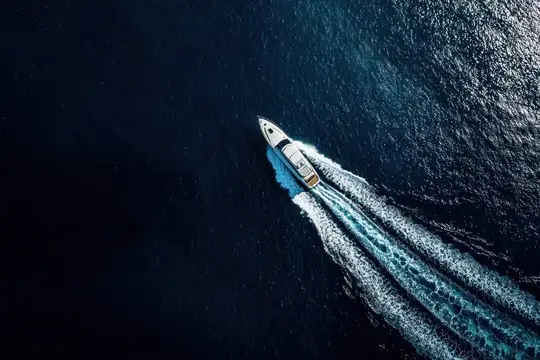 Белая моторная яхта оставляет пенный след на тёмной воде
