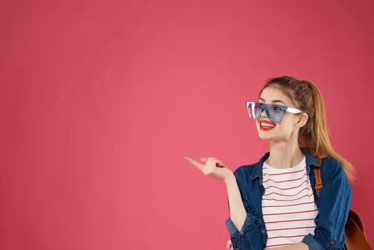Улыбающаяся девушка в очках указывает пальцем на розовом фоне