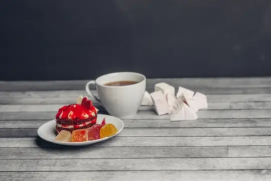 Чашка кофе с пирожным и кусочками рахат-лукума на деревянном столе