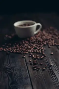 Белая чашка кофе и рассыпанные зерна на темном дереве