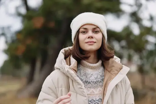 Молодая женщина в белой шапке и пуховике на осенней прогулке