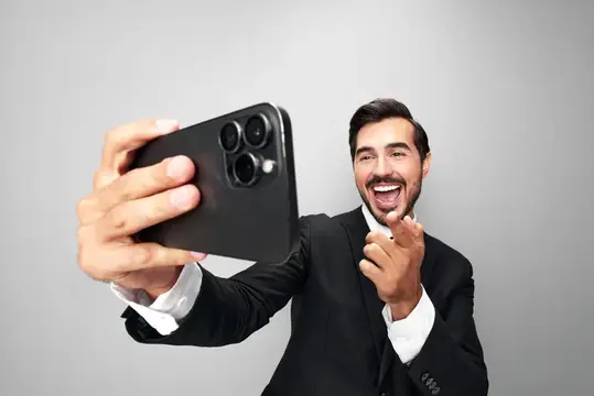 Улыбающийся бородатый мужчина в костюме делает селфи на смартфон