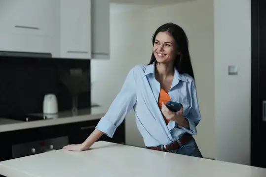 Улыбающаяся темноволосая женщина с пультом на светлой кухне