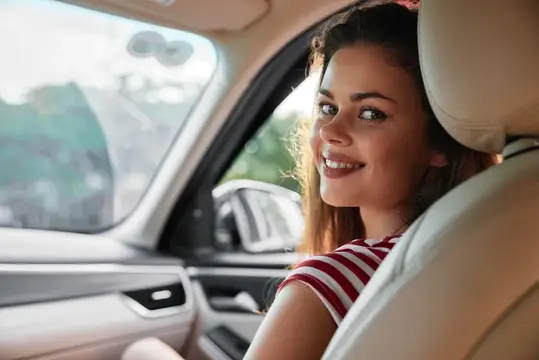 Улыбающаяся темноволосая девушка в полосатой футболке в салоне автомобиля