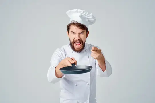 Разъяренный бородатый повар с сковородой грозит кулаком