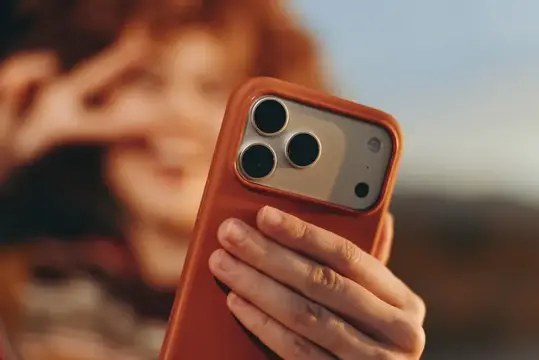 Рыжеволосая девушка держит оранжевый смартфон с тремя камерами