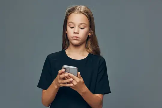 Юная девушка в черной футболке сосредоточенно смотрит на экран телефона