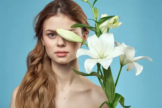 Рыжеволосая девушка с белыми лилиями у лица на голубом фоне