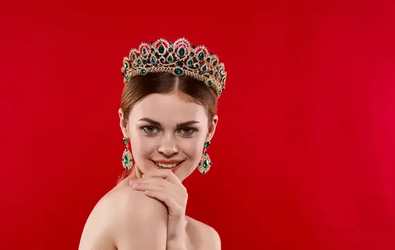 Портрет уверенной женщины на красном фоне с короной на голове и серьгами в ушах