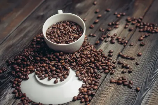 Белая чашка с кофейными зёрнами на тёмном деревянном столе