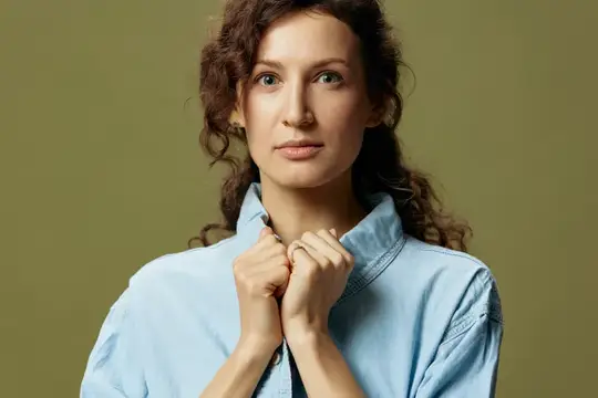 Серьезная очаровательная кудрявая красивая девушка в джинсах и повседневной рубашке прикасается к воротнику, смотрит в камеру, позирует изолированно на оливково-зеленом фоне