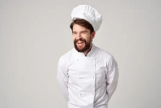 Улыбающийся бородатый повар в белом колпаке на сером фоне
