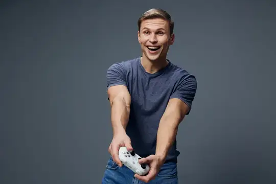 Улыбающийся парень в футболке играет в видеоигру на сером фоне
