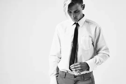 Молодой мужчина в белой рубашке заправляет её в брюки