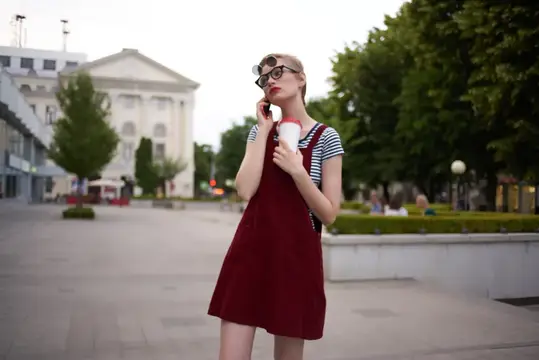 Молодая женщина в очках с кофе разговаривает по телефону на городской площади