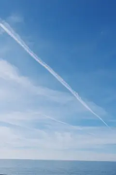 Белый след самолёта в ясном небе над морем