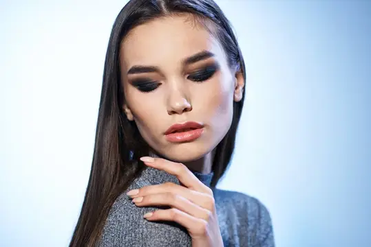 Молодая женщина с длинными тёмными волосами и макияжем смотрит вниз