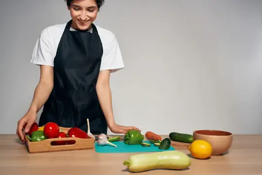 Улыбающаяся девушка в фартуке раскладывает свежие овощи на кухне