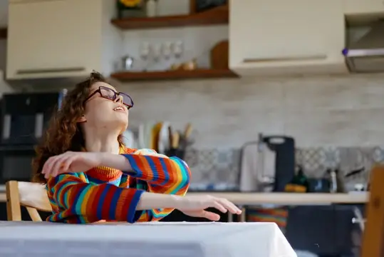 Кудрявая девочка в очках танцует за столом на кухне