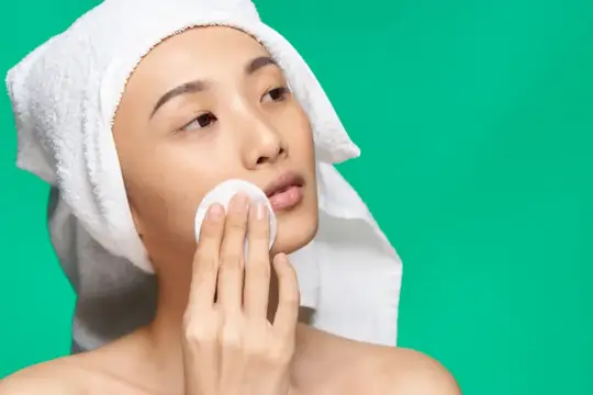 Азиатская женщина с обнажёнными плечами и чистой кожей снимает макияж