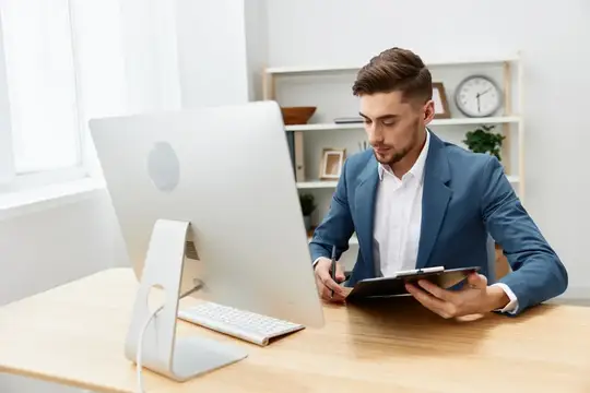 Молодой мужчина в синем пиджаке работает за компьютером в офисе