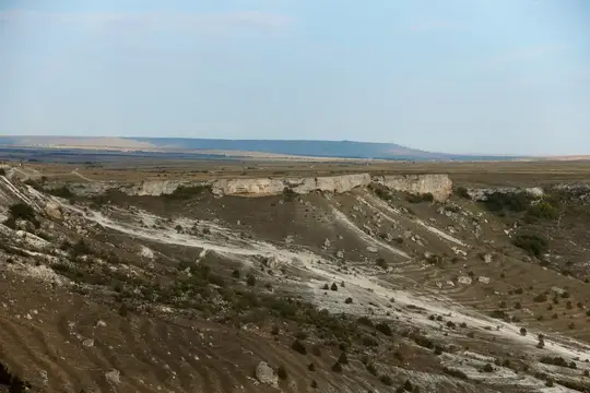 Скалистый склон с белыми обрывами и редкими кустами под ясным небом