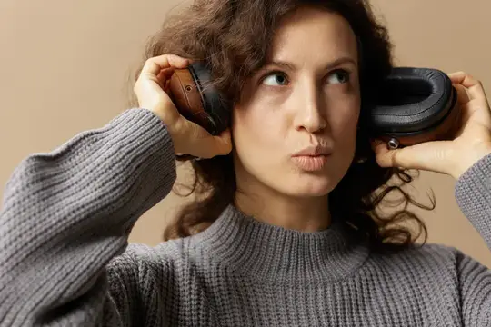 Кудрявая девушка в сером свитере снимает наушники
