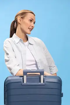 Улыбающаяся светловолосая женщина с чемоданом на голубом фоне