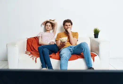 Скучающая пара с попкорном смотрит телевизор на диване